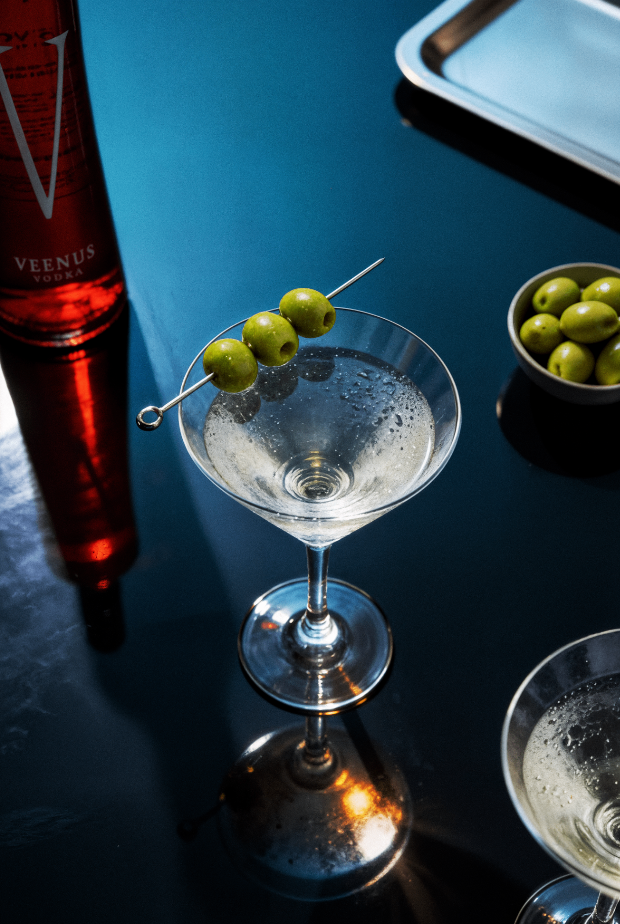 Martini glass with olives next to Veenus Vodka bottle